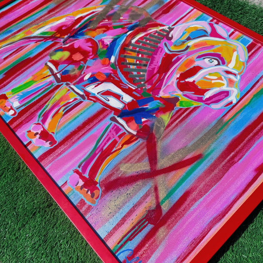 Colorful abstract painting on a mat with a red border, displayed on grass.