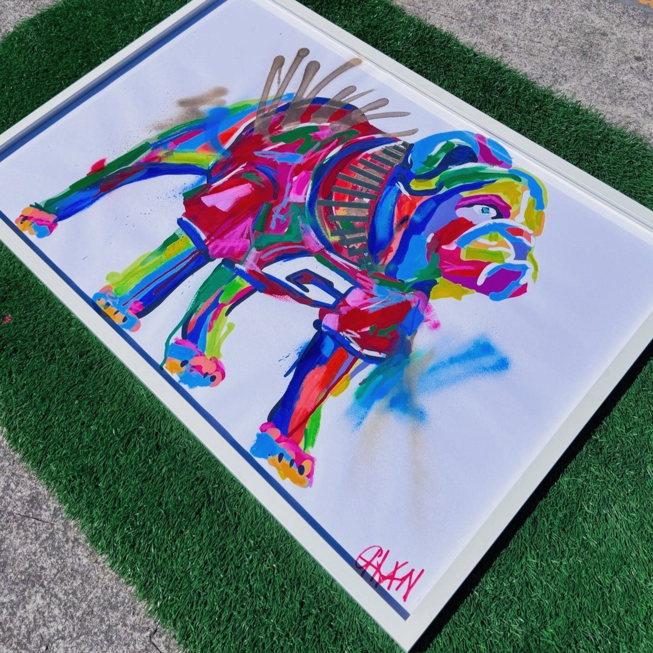 Colorful abstract dog painting on a white background, placed on a green grassy surface.